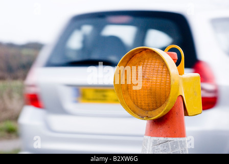 Auto passando una luce gialla lampeggiante sulla parte superiore di un cono in lavori stradali nel Regno Unito Foto Stock