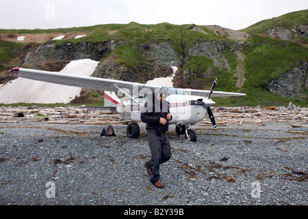 Pilota nella parte anteriore del suo aereo su un driftwood spiaggia coperta nel Parco Nazionale e Riserva di Katmai, Alaska, USA Foto Stock