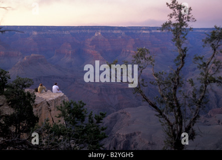 Un uomo e una donna si siedono sul bordo del Grand Canyon al tramonto Foto Stock