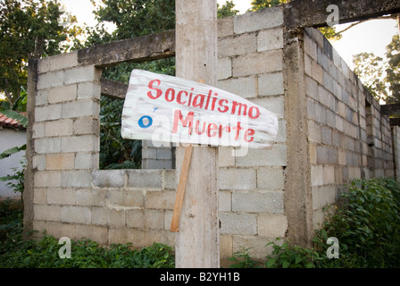 La morte o il socialismo segno di fronte all edificio incompiuto costruzione con erbacce crescente Cuba Foto Stock