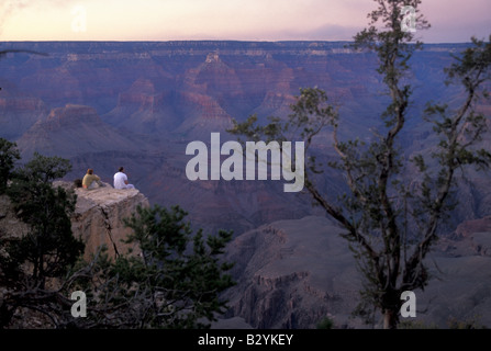 Un uomo e una donna si siedono sul bordo del Grand Canyon al tramonto Foto Stock