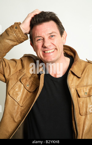 L uomo nella sua 40s sorridente indossa una giacca di pelle - la mano sulla testa Foto Stock