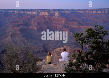 Un uomo e una donna si siedono sul bordo del Grand Canyon al tramonto Foto Stock