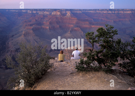 Un uomo e una donna si siedono sul bordo del Grand Canyon al tramonto Foto Stock