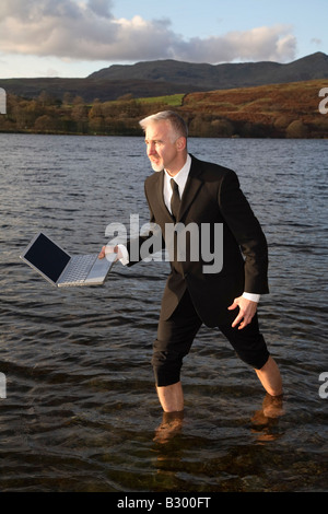 Imprenditore a piedi attraverso il lago con il computer portatile Foto Stock