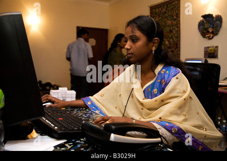 Un dipendente in Bangalore colloqui su un auricolare mentre lavora sul suo computer in un ufficio di piccole dimensioni. Foto Stock