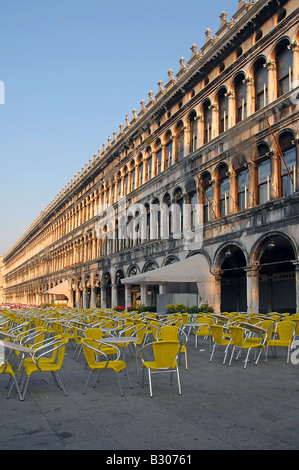 Le Procuratie Vecchie con tavoli e sedie di colore giallo in Piazza San Marco a sunrise Foto Stock