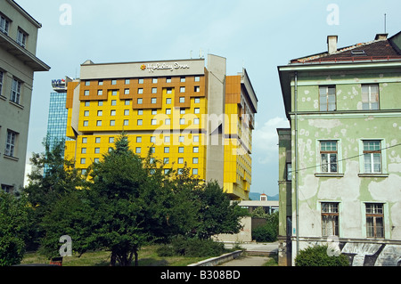 La Bosnia, Sarajevo. Sarajevo Holiday Inn su 'Sniper Alley recentemente ridipinto accanto a pesantemente case danneggiate dalla guerra Foto Stock