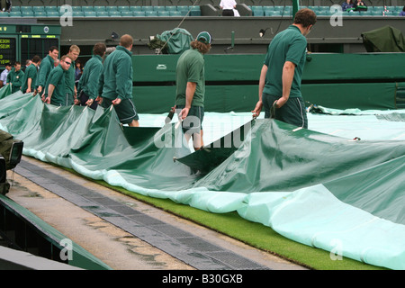 Il personale di terra preparare per rimuovere il coperchio sul Centre Court dopo una pioggia di ritardo al Wimbledon Tennis Championship in Inghilterra Foto Stock
