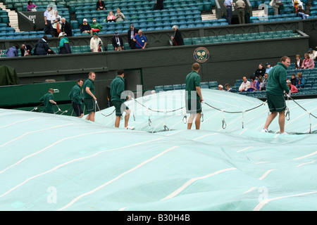 Il personale di terra preparare per rimuovere il coperchio sul Centre Court dopo una pioggia di ritardo al Wimbledon Tennis Championship in Inghilterra Foto Stock