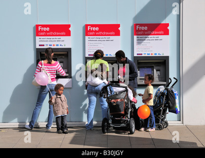 Una famiglia con carrozzine, bambini e un bambino, tenendo palloncini, con una singola femmina, utilizzando HSBC Bank le macchine di contanti a Kingston, Regno Unito Foto Stock