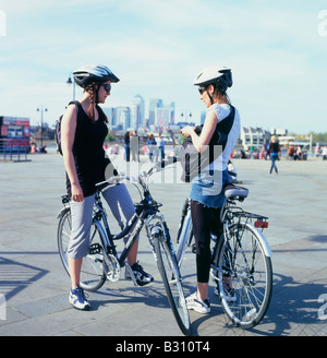 I ciclisti femmina sms sul cellulare a Greenwich con Canary Wharf in distanza Londra UK KATHY DEWITT Foto Stock