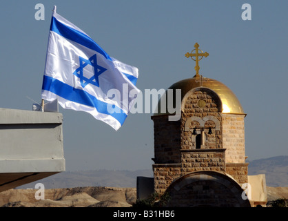 Una bandiera Israeliana vola al vento nella parte anteriore di una chiesa ortodossa greca sul Fiume Giordano sulla sponda opposta a Gerico, Israele. Foto Stock