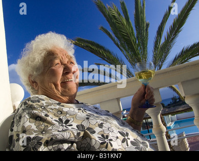 Donna anziana si rilassa con soddisfazione al sole con un bicchiere di vino bianco nella sua villa per le vacanze home Foto Stock