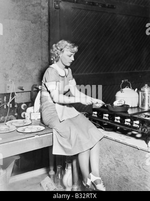 Giovane donna seduta sul contatore e la cottura di alimenti in cucina Foto Stock