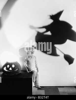 Ragazzo seduto su una tabella con una zucca e un'ombra di una strega su una parete Foto Stock