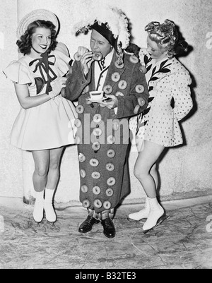 Uomo in un abito fatto di ciambelle in piedi tra due ragazze adolescenti Foto Stock