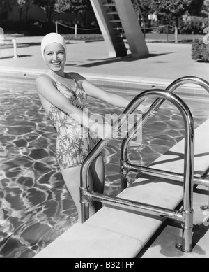 Giovane donna a salire la scala di una piscina Foto Stock