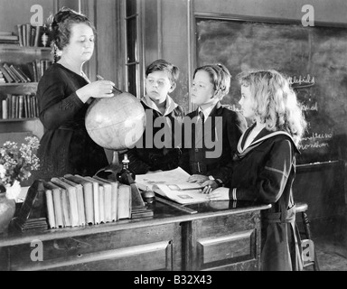 Insegnante in un aula con tre studenti che puntano a un globo Foto Stock