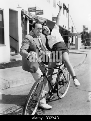 Uomo cercando di trovare il giusto equilibrio tra un esuberante donna su una bicicletta Foto Stock