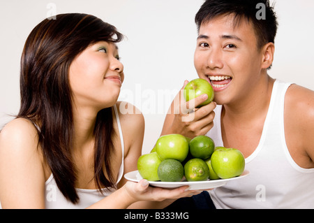 Un giovane maschio asiatici felicemente mangia una mela verde a lui offerto dalla sua bella ragazza Foto Stock