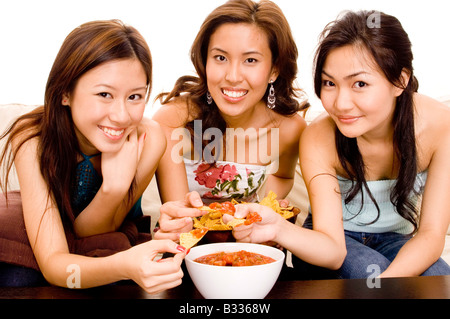 Tre Pretty donne asiatiche mangiare nachos e salsa dip Foto Stock