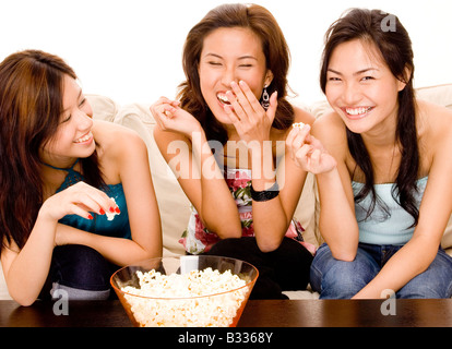 Tre attraenti donne asiatiche divertiti a mangiare popcorn Foto Stock