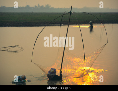 Laos Ventiane fiume Mekong donne la pesca con luce reti da pesca su una canna da pesca in piedi in acqua al tramonto Foto Stock