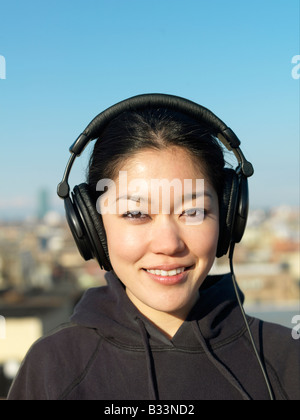 Un ritratto di una giovane donna asiatica che indossa le cuffie e ascolto di musica. Foto Stock