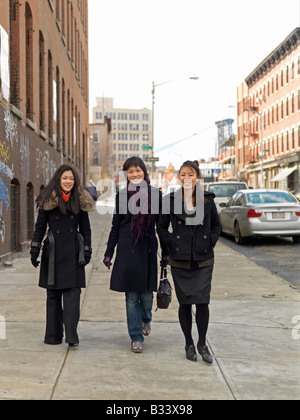 Tre giovani donne asiatiche a piedi lungo una strada di città durante la stagione invernale a conversare e ridere Foto Stock