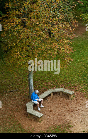 Maschio di lettura su una panchina nel parco sotto un albero di Rocamadour, Francia UE. Foto Stock