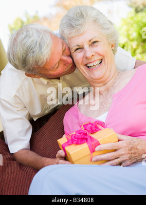 Il marito dando moglie dono sul patio bacia e sorridente Foto Stock