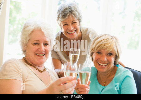 Tre donne in salotto a bere champagne e sorridente Foto Stock