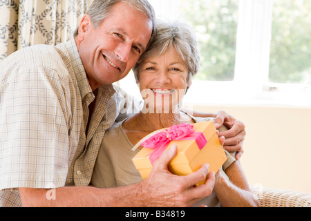 Il marito dando moglie dono nel soggiorno sorridente Foto Stock