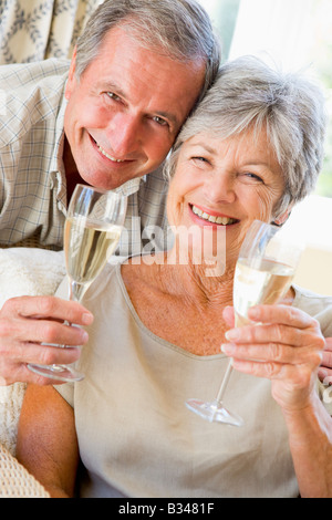 Matura in soggiorno a bere champagne e sorridente Foto Stock