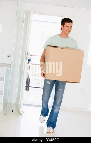 Uomo con scatola in movimento nella nuova casa sorridente Foto Stock