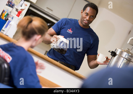 Tre i vigili del fuoco in sala pausa con uno ottenere caffè (messa a fuoco selettiva) Foto Stock