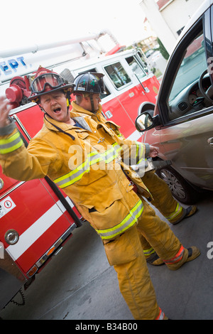Vigile del fuoco di movimentazione per il backup con un altro pompiere utilizzando le ganasce della vita su una porta di cabina (sfocatura) Foto Stock