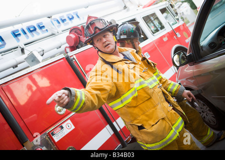 Fireman rivolti a qualcosa con un altro pompiere utilizzando le ganasce della vita sulla portiera di una macchina Foto Stock