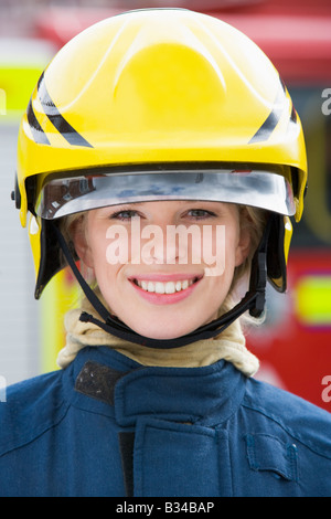 Firewoman in piedi dal motore Fire indossando il casco Foto Stock