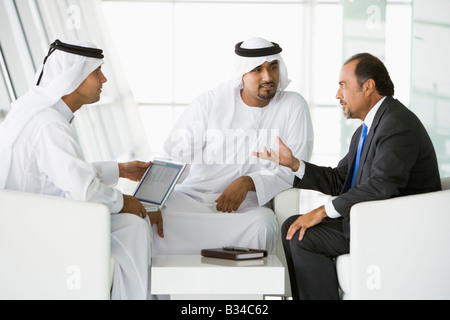 Tre uomini di affari interni con un laptop parlando (alta chiave/messa a fuoco selettiva) Foto Stock