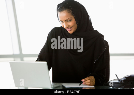 Imprenditrice in ufficio con computer portatile iscritto e sorridente (alta chiave/messa a fuoco selettiva) Foto Stock