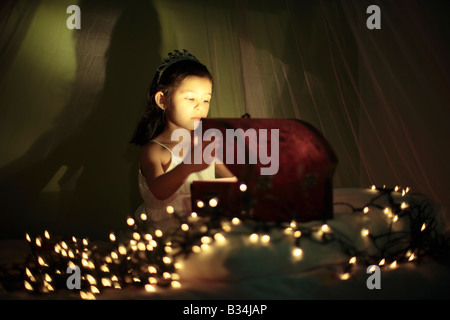 Il magico scrigno bambina di cinque anni si siede sul letto con baldacchino e apre una scatola Foto Stock