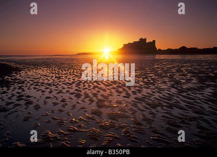 Il sole sorge su Bamburgh Castle e la spiaggia sulla costa di Northumberland dell'Inghilterra Foto Stock