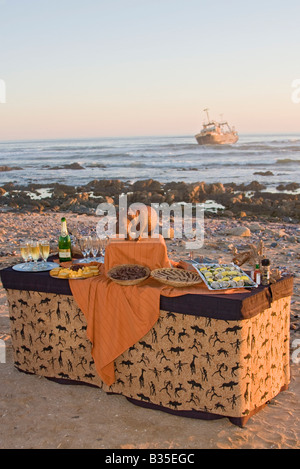 Sundown aperitivi serviti sulla spiaggia di Swakopmund Namibia con il relitto del peschereccio Kolmanskop appena offshore Foto Stock