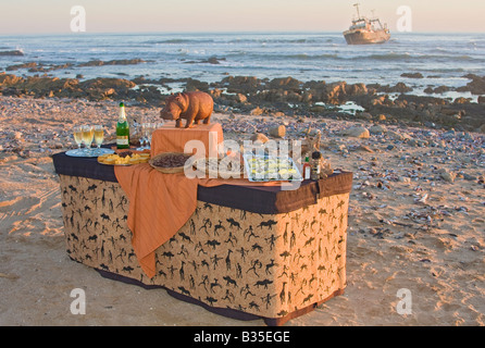 Sundown aperitivi serviti sulla spiaggia di Swakopmund Namibia con il relitto del peschereccio Kolmanskop appena offshore Foto Stock