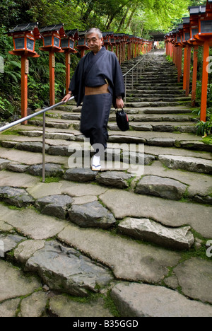 Uomo che indossa estate accappatoi Yukata scende di gradini di pietra passato lanterne rosse al Santuario Kibune vicino Kyoto Foto Stock