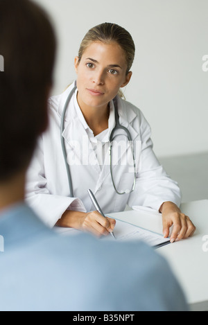 Medico iscritto alla scrivania, paziente in primo piano Foto Stock