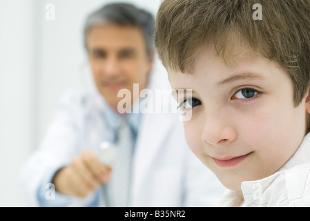 Ragazzo che sorride alla telecamera, medico tenendo uno stetoscopio in background Foto Stock