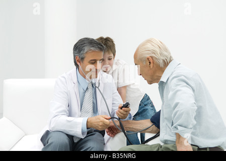 Medico senior di misurazione dell'uomo pressione sanguigna, ragazzo guardando Foto Stock